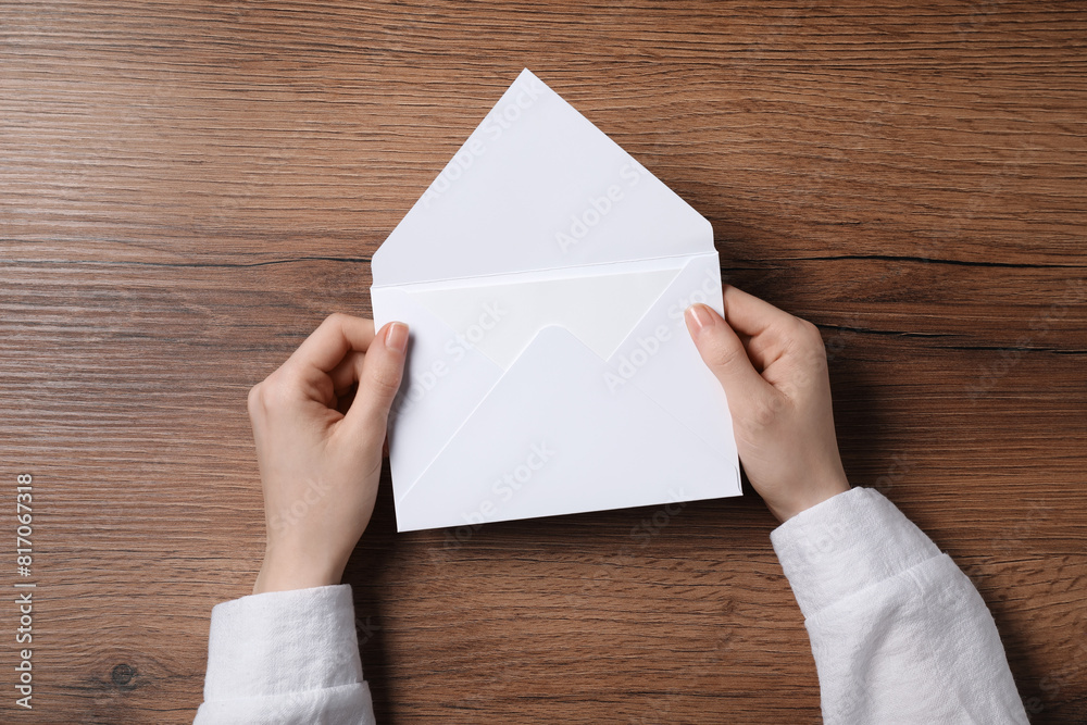 Woman holding letter envelope with card at wooden table, top view Woman holding letter envelope with card at wooden table, top view