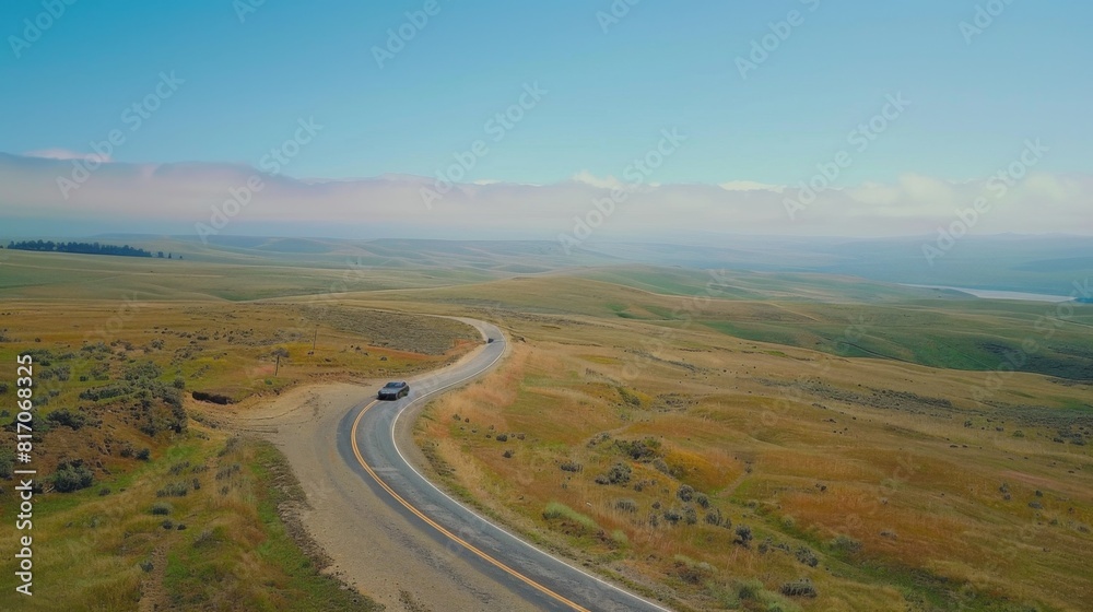 Aerial view of a winding road through picturesque countryside, with a car cruising along under a blue sky