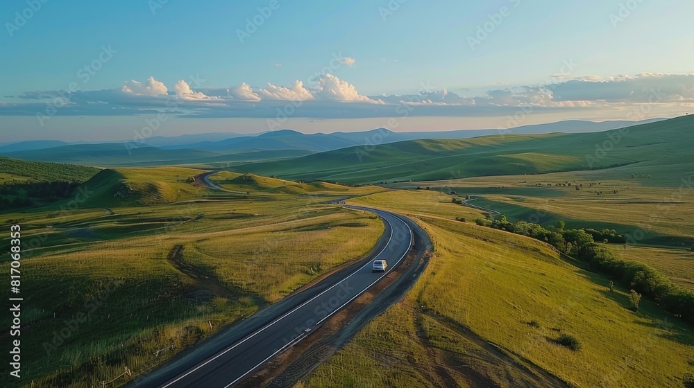 Aerial view of a winding road through picturesque countryside, with a car cruising along under a blue sky Aerial view of a winding road through picturesque countryside, with a car cruising along under a blue sky