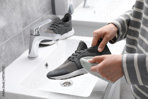 Woman washing stylish sneakers with brush in sink  closeup