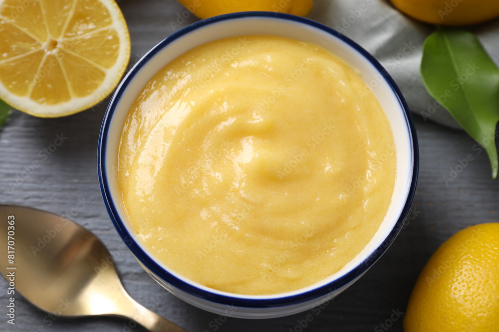 Delicious lemon curd in bowl, fresh citrus fruits, green leaf and spoon on grey wooden table, closeup Delicious lemon curd in bowl, fresh citrus fruits, green leaf and spoon on grey wooden table, closeup