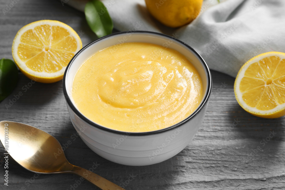 Delicious lemon curd in bowl, fresh citrus fruits and spoon on grey wooden table, closeup Delicious lemon curd in bowl, fresh citrus fruits and spoon on grey wooden table, closeup