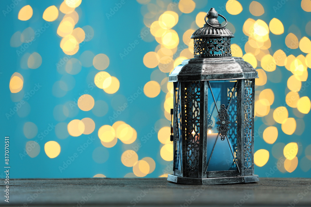 Traditional Arabic lantern on wooden table against light blue background with blurred lights. Space for text