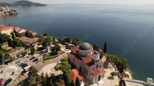 Gliding above the picturesque town of Kavala, Greece, the camera captures stunning vistas of colorful buildings, cobblestone streets, bustling markets, and the sparkling blue ocean