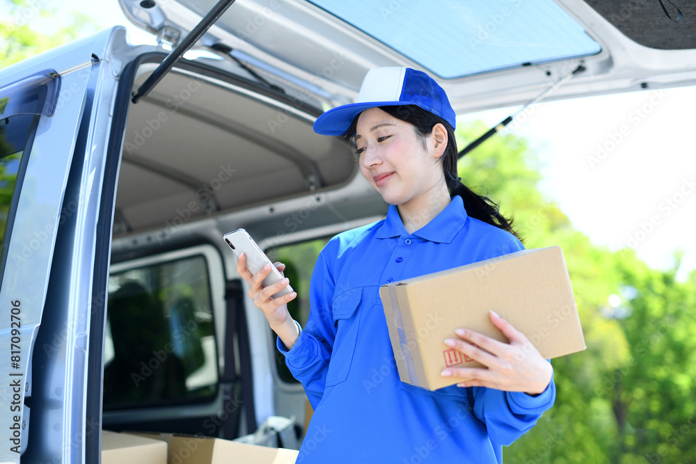 荷物を持ちスマホを見る配送ドライバー女性 荷物を持ちスマホを見る配送ドライバー女性