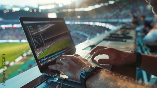 A man, likely a sports journalist, is typing on a laptop in front of a stadium