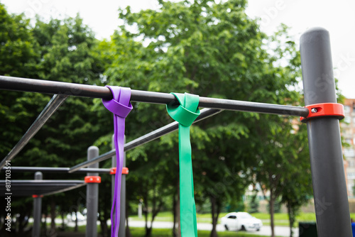 Purple and green Elastic rubber bands for exercise tied on a horizontal bar . Close up view . Horizontal shot .