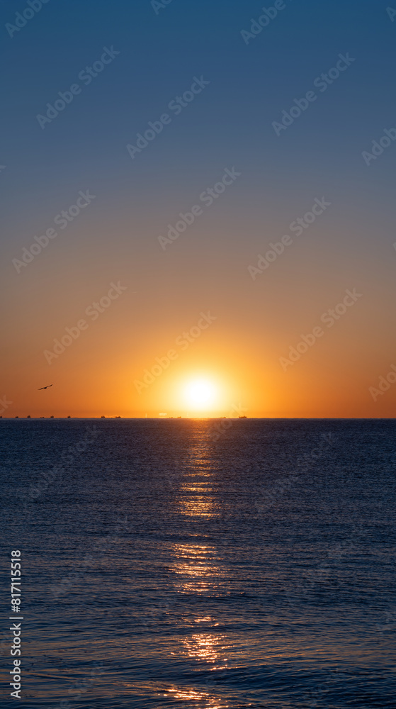 Idyllic sunrise with the bright sun emerging on the sea horizon beautifully illuminating the calm blue waters of the Mediterranean Sea with silhouettes of fishing boats and seagulls on the horizon. Idyllic sunrise with the bright sun emerging on the sea horizon beautifully illuminating the calm blue waters of the Mediterranean Sea with silhouettes of fishing boats and seagulls on the horizon.