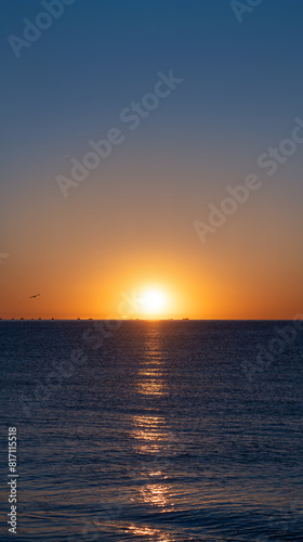 Idyllic sunrise with the bright sun emerging on the sea horizon beautifully illuminating the calm blue waters of the Mediterranean Sea with silhouettes of fishing boats and seagulls on the horizon. © sirbouman