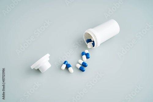 Blue and white capsules spilled out of a medicine jar on a blue background.