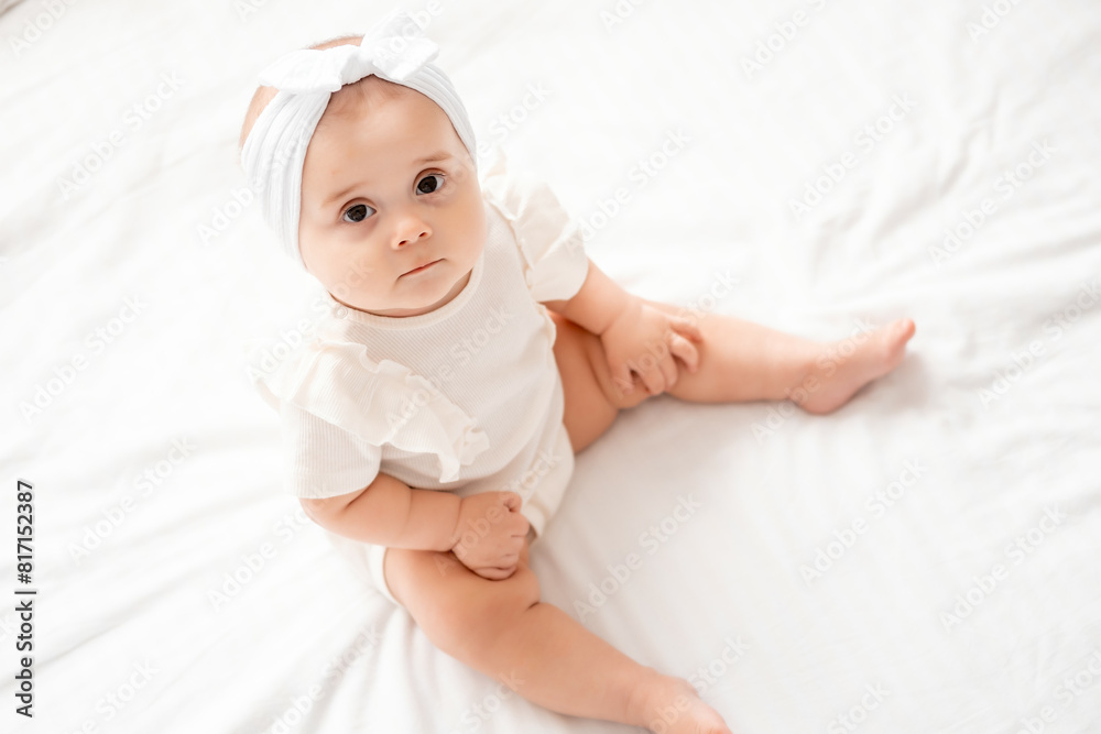 newborn baby girl looks up sitting on a bed in white clothes in newborn baby girl looks up sitting on a bed in white clothes in