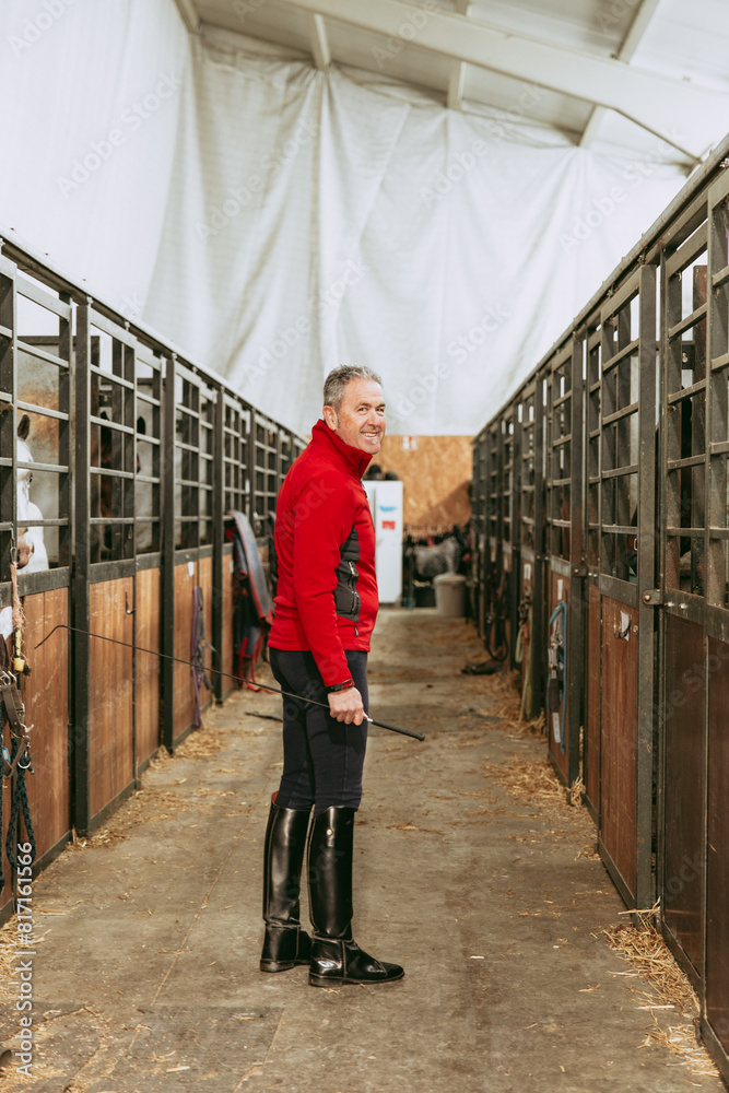 Smiling rider ready to mount in stable aisle. Smiling rider ready to mount in stable aisle.