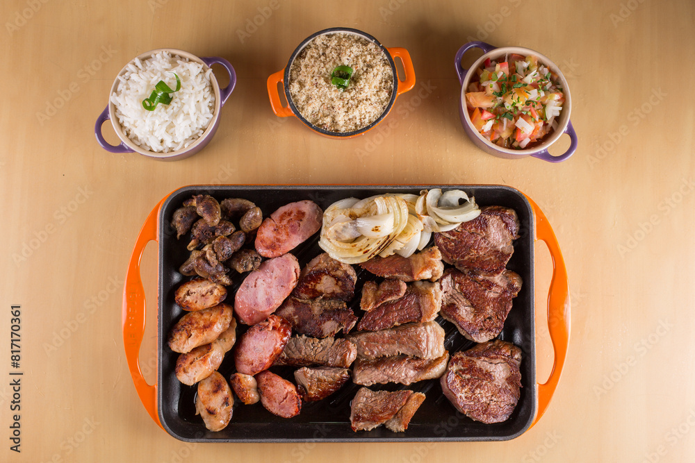 Picanha, a traditional cut of Brazilian meat, served with grilled onion and sausage on a hot iron plate. Brazilian barbecue served on a hot iron plate accompanied by rice, farofa and vinaigrette sauce Picanha, a traditional cut of Brazilian meat, served with grilled onion and sausage on a hot iron plate. Brazilian barbecue served on a hot iron plate accompanied by rice, farofa and vinaigrette sauce