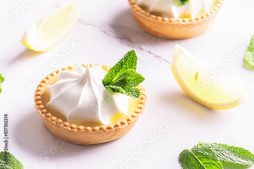 Aromatic homemade lemon tartlets with cream and mint leaves on white marble table close up.