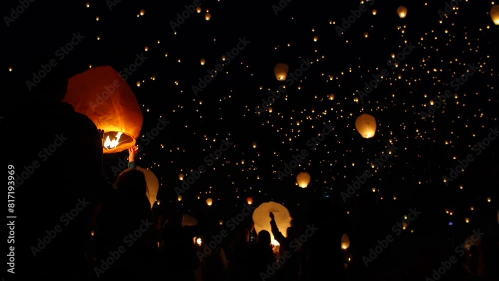 Silhouette of crowd releasing Chinese lanterns into night sky