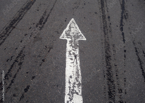 white painted pointing arrow on asphalt road with wet tyres tracks.