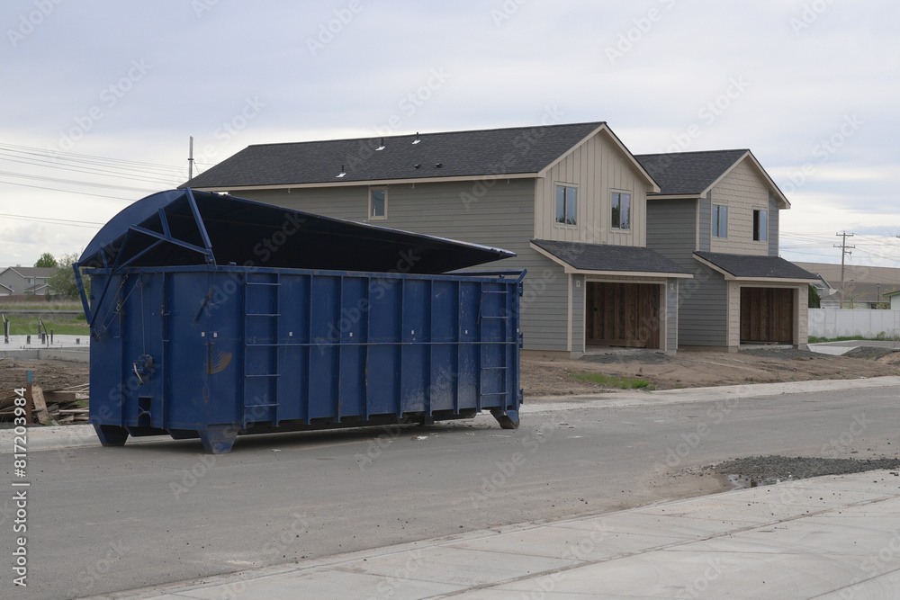 Large blue construction dumpster in front of new duplex homes under construction. Large blue construction dumpster in front of new duplex homes under construction.