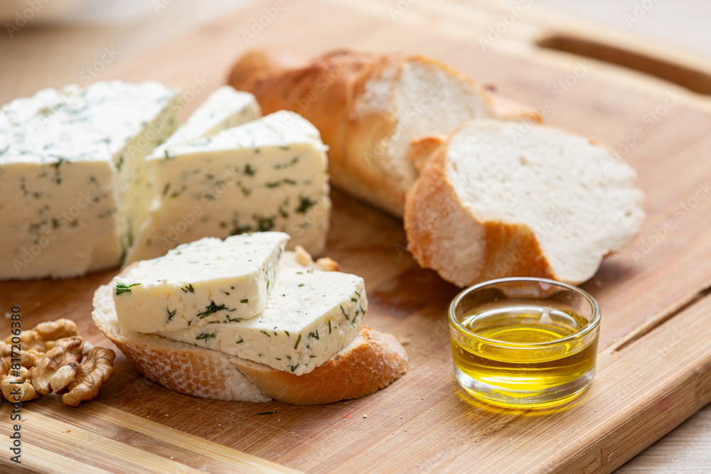 Variety of home made cheese and herbs, olive oil, and bread on a wooden board. Brined curd white cheese with vegetables on the table Variety of home made cheese and herbs, olive oil, and bread on a wooden board. Brined curd white cheese with vegetables on the table
