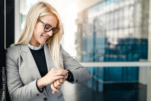 Smiling businesswoman checking the time on her watch while standing outside her office in modern corporative center and waiting for a business meeting to begin.