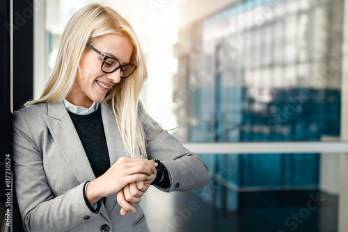 Εκτύπωση καμβά Smiling businesswoman checking the time on her watch while standing outside her office in modern corporative center and waiting for a business meeting to begin