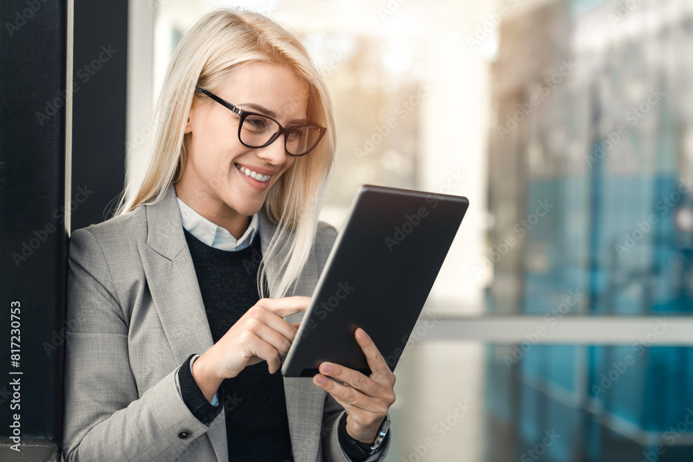CEO female white collar worker with glasses using digital tablet while standing outside the office. CEO female white collar worker with glasses using digital tablet while standing outside the office.