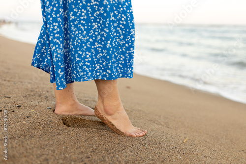 Woman in dress walking on sand beach. Wave motion coming to the foot, foaming sea texture. Summer and vacation concept. © mdyn