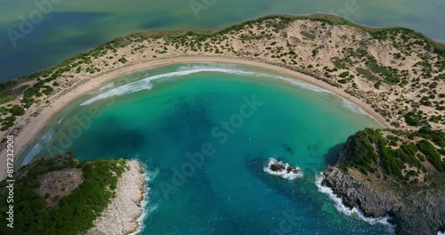 Captured from above, this stunning view showcases the crescent-shaped Voidokilia Beach in Greece. The clear turquoise waters, surrounded by sandy shores and lush greenery, photo