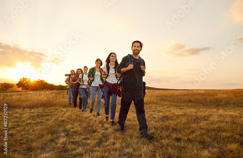 Team of tourists enjoying beauty of nature on trekking or hiking tour in countryside in autumn. Group of happy healthy male and female hikers with backpacks walking through field in morning or evening