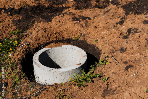 A concrete pipe section partially buried in soil, surrounded by vegetation and dry ground, in an outdoor construction site. The infrastructure project is in a rural landscape photo