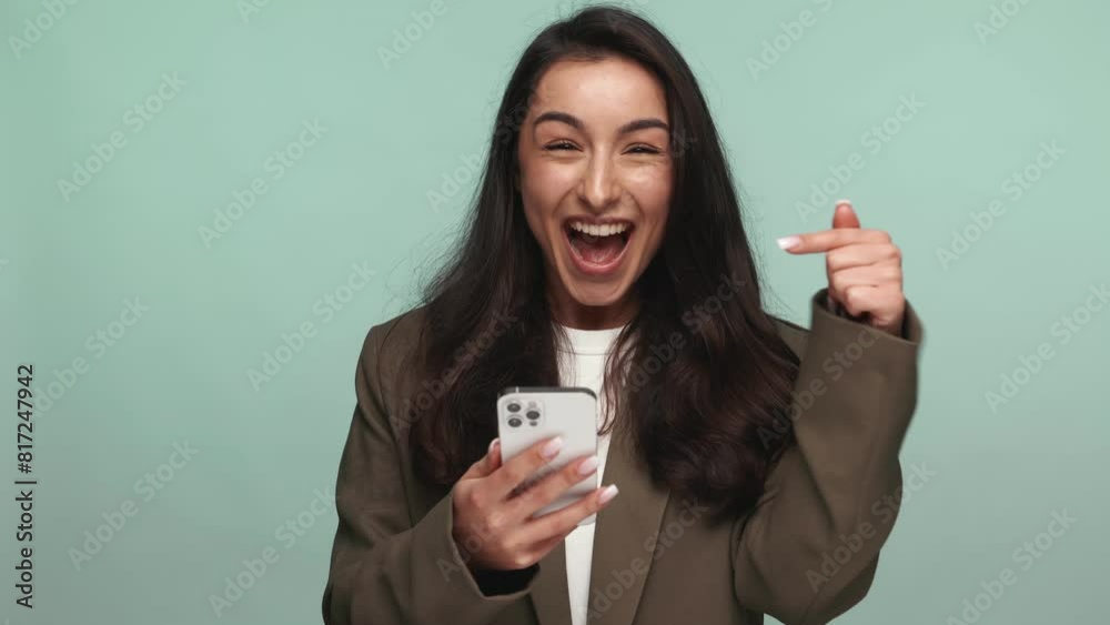 Joyful woman in business attire celebrates a victory on her smartphone, expressing happiness and success. Joyful woman in business attire celebrates a victory on her smartphone, expressing happiness and success.