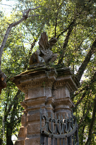 Obraz na płótnie In the summer park there is an ancient stone high gate with an iron lattice, on top there is a statue of a dragon, vertical view w salonie