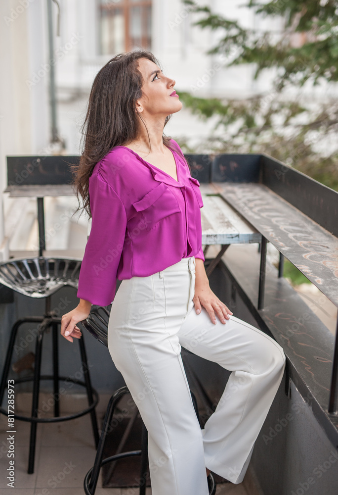 Beautiful young brunette woman in a purple blouse and white pants posing outdoor. Portrait of a beautiful young brunette woman with long hair posing fashion