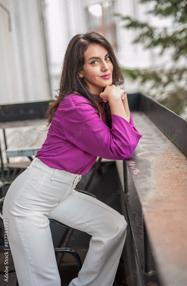 Beautiful young brunette woman in a purple blouse and white pants posing outdoor. Portrait of a beautiful young brunette woman with long hair posing fashion