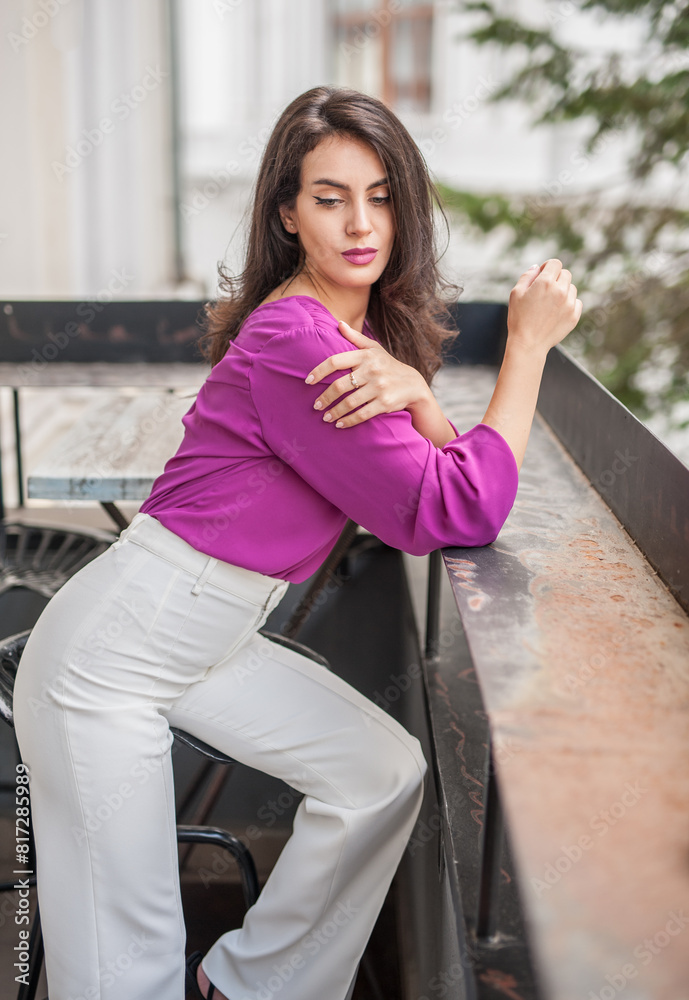 Beautiful young brunette woman in a purple blouse and white pants posing outdoor. Portrait of a beautiful young brunette woman with long hair posing fashion