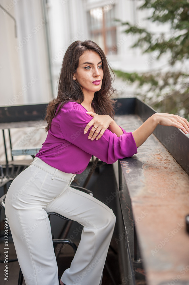 Beautiful young brunette woman in a purple blouse and white pants posing outdoor. Portrait of a beautiful young brunette woman with long hair posing fashion