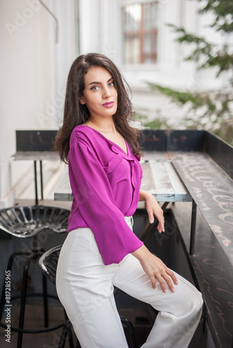 Obraz na płótnie Beautiful young brunette woman in a purple blouse and white pants posing outdoor. Portrait of a beautiful young brunette woman with long hair posing fashion w salonie