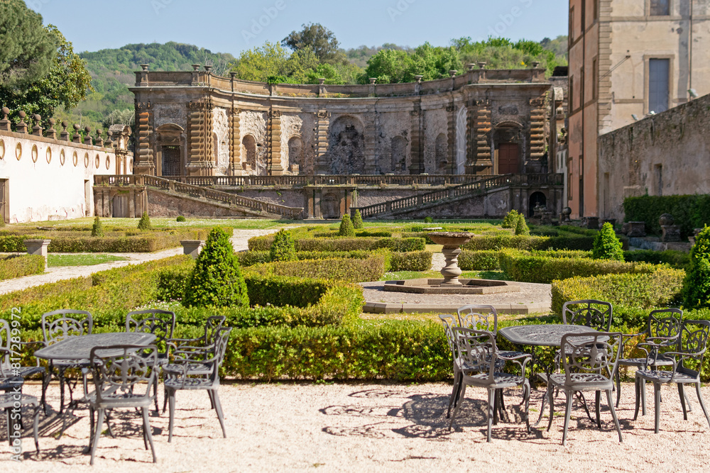 A beautiful summer park with figured trees and paths in the courtyard of an ancient villa, fenced with an ancient stone wall with sculptures, there is figured garden furniture made of metal