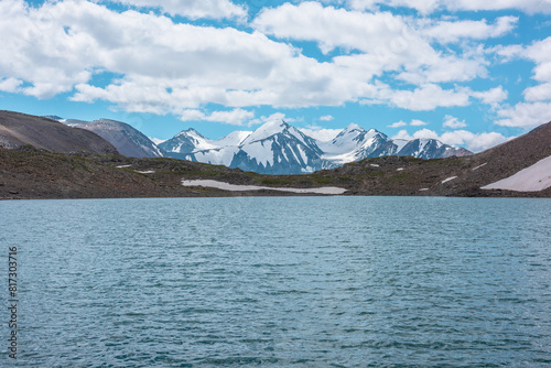 Closeup of ripples on shiny azure water surface of mountain lake against three snowy peaked tops. Nature background of turquoise alpine lake and snow-covered range with few most beautiful pointy peaks