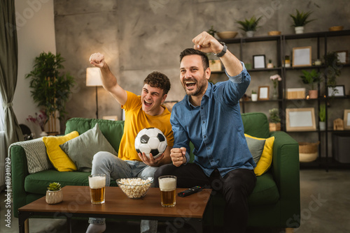 Young and adult man friends watch football match and cheer at home © Miljan Živković