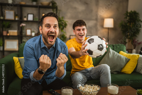 Young and adult man friends watch football match and cheer at home © Miljan Živković