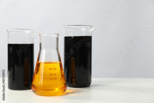 Beakers and flask with different types of oil on white table, space for text