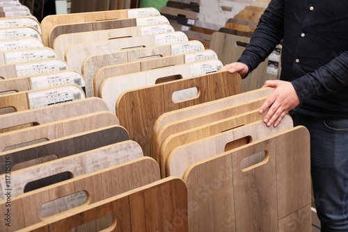 Man choosing wooden flooring among different samples in shop, closeup