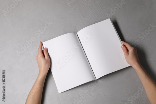 Woman holding open notebook with blank pages at light grey table, top view. Mockup for design