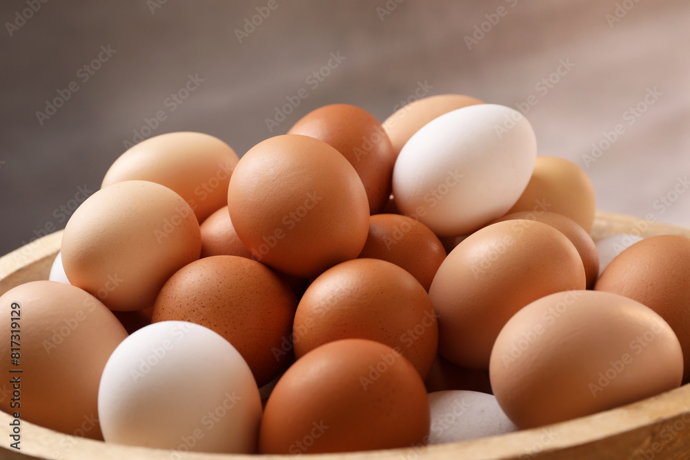 Fresh chicken eggs in bowl on light brown background, closeup