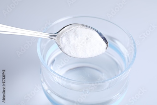 Adding baking soda into glass of water on light background, closeup