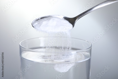 Adding baking soda into glass of water on light grey background, closeup photo
