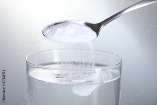 Fotografía Adding baking soda into glass of water on light grey background, closeup