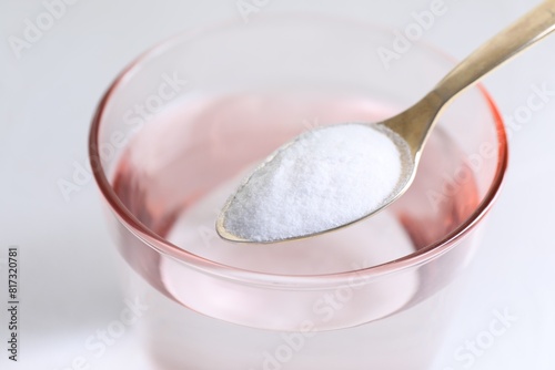 Spoon with baking soda over glass of water on white background, closeup