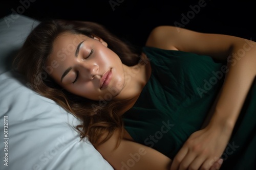 Beautiful woman sleeping in bed on her stomach She is in a dark green nightgown She is facing the camera Her eyes are closed