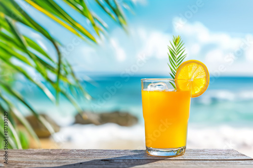 Refreshing orange juice in a glass with ice cubes on a rustic wooden table overlooking a tropical beach